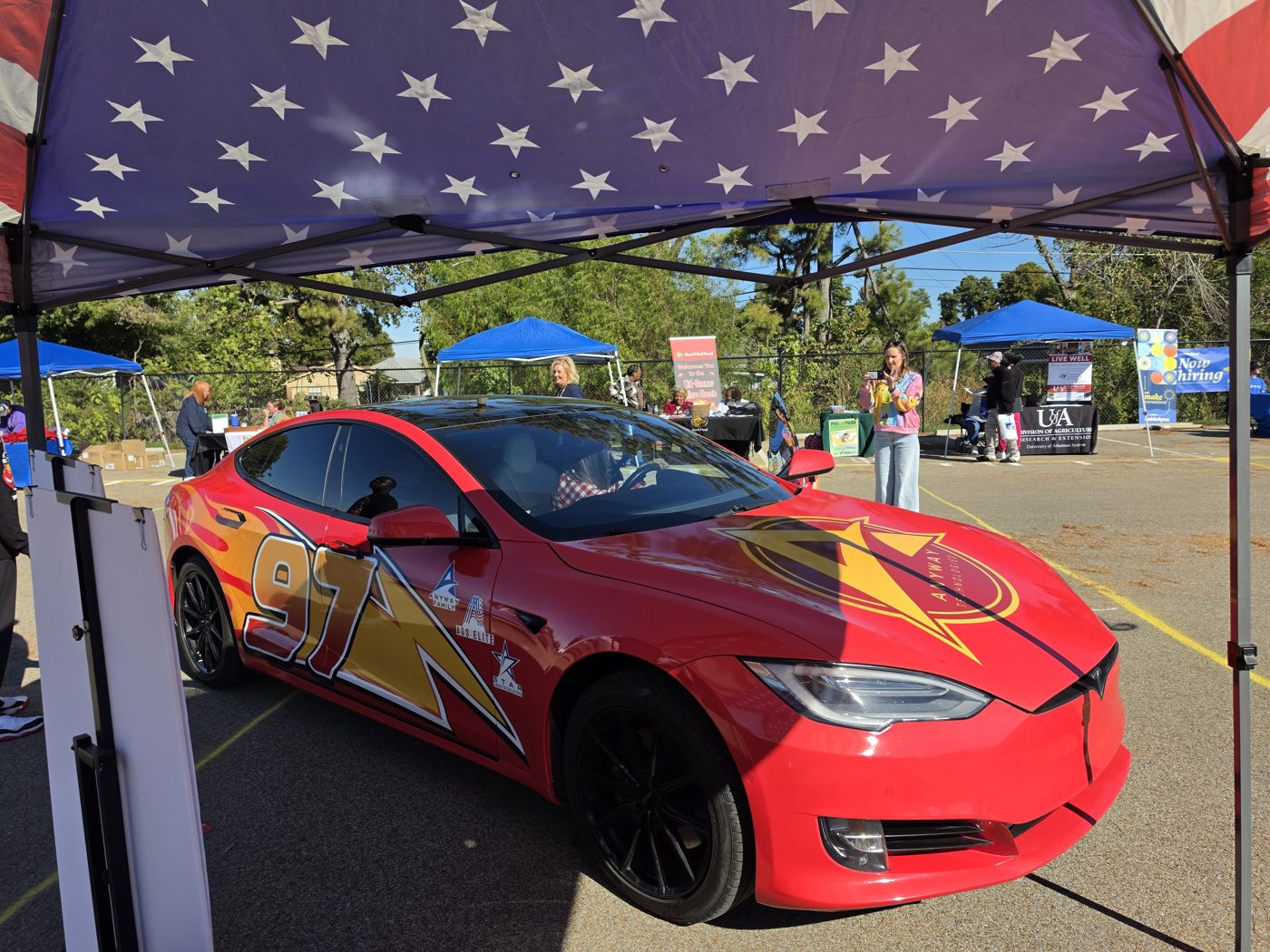 Kachow, a red and yellow wrapped AnyWay Technologies car, parked under a tent at a community event